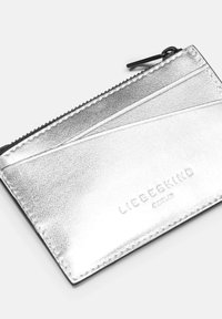 Srebrny metaliczny etui na karty o teksturowej powierzchni, z zamknięciem na zamek błyskawiczny i wytłoczonym logo, w kątem nachylonym do kart, z czarnym wykończeniem brzegów.