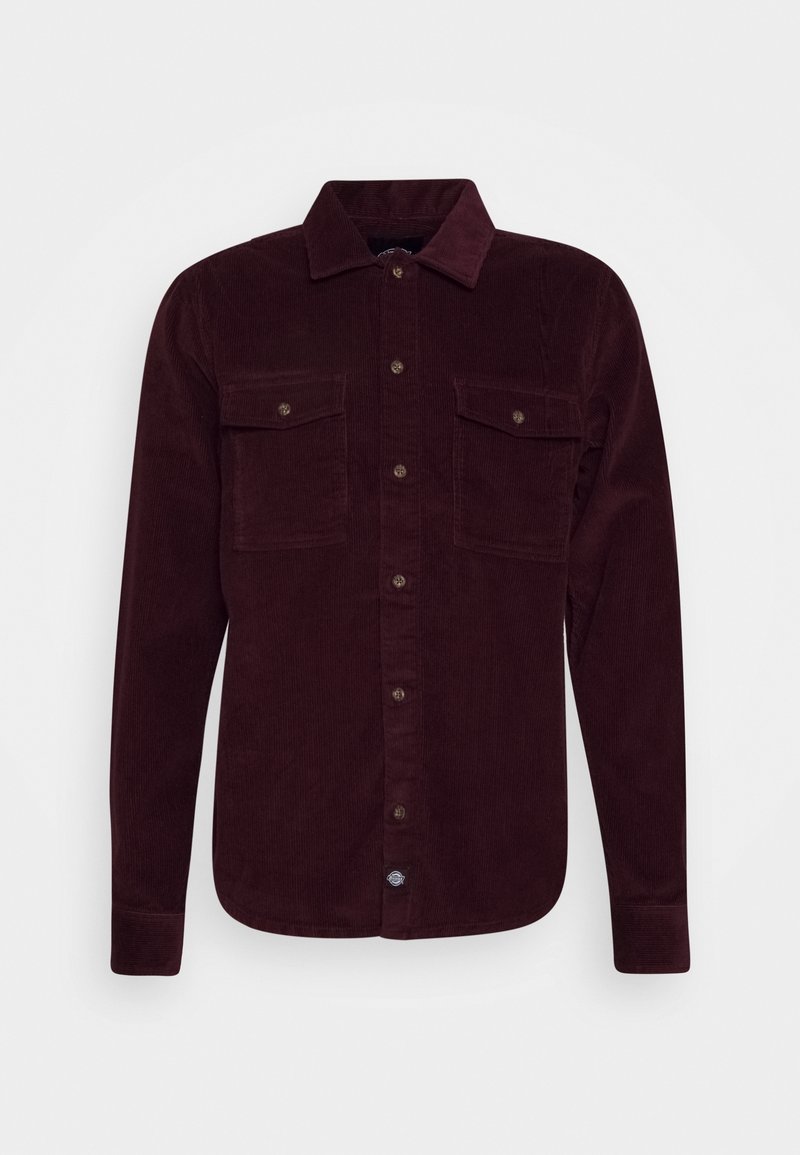 Burgunderfärgad kordflossskjorta med långa ärmar, knäppning framtill, två bröstfickor och krage. Har strukturerad tyg och kontrasterande knappar.
