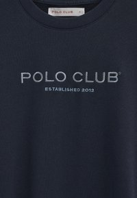 Marineblåt tøj med "POLO CLUB" broderet i store bogstaver og "ESTABLISHED 2012" nedenunder i mindre tekst.