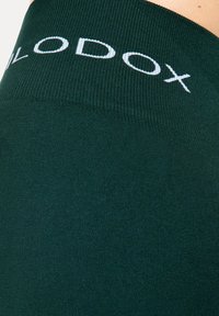 Donkergroene legging met een geribbelde textuur en een brede tailleband met de merknaam "LOD" in witte letters.