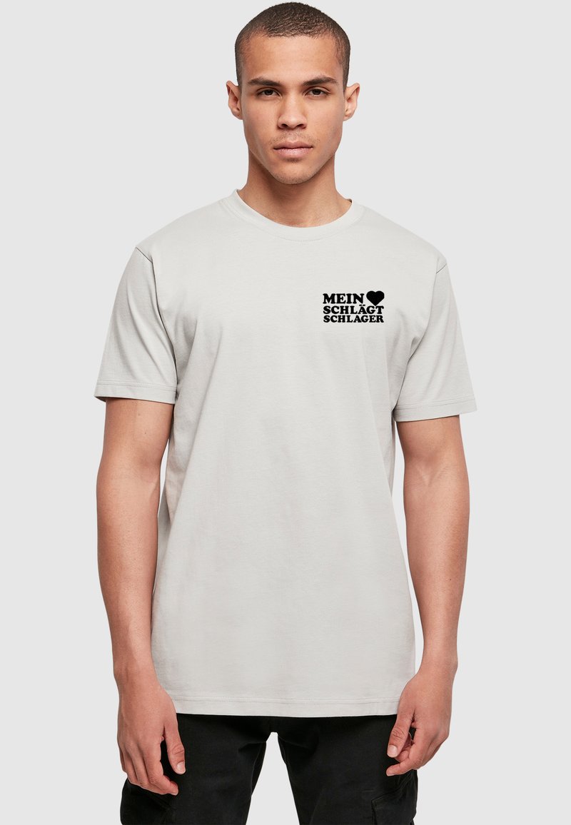 Lysegrå bomulds t-shirt med korte ærmer og rund halsudskæring. Har sort trykt tekst på venstre brystområde. Renssym, enkelt design.