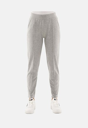 Pantalon de survêtement slim gris clair avec coutures avant, poches latérales et ceinture élastique, porté avec des baskets blanches sur fond blanc.