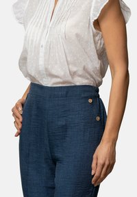Camisa blanca con texturas sutiles y pliegues, combinada con pantalones azul oscuro que tienen un acabado suave y dos botones decorativos en la cintura.