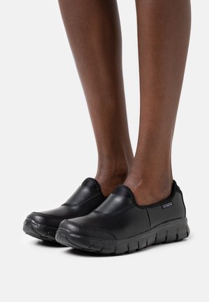 Des chaussures noires à enfiler avec une tige en cuir lisse, des accents texturés et une semelle en caoutchouc souple et rembourrée conçue pour le confort.