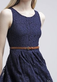 Navy kanten jurk met een getailleerde bovenkant en een uitlopende rok, voorzien van een bruine leren riem rond de taille. Textuur met bloemenpatroon overal.
