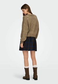 Strik beige sweater med åbent maskemønster, parret med en plisseret marineblå og brunternet nederdel, samt brune støvler til midt på læggen med spænder.