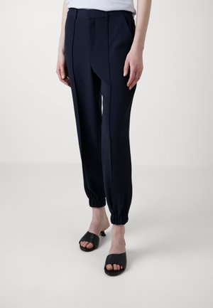 Marineblauwe tapered broeken met elastische boorden, met een gladde textuur en geplooide voorkant. Gecombineerd met zwarte openstaande muiltjes.