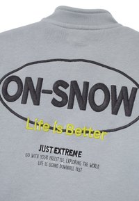 Sudadera gris con texto bordado en negro y amarillo "ON-SNOW Life is Better" y "JUST EXTREME" en la parte posterior, que cuenta con un escote redondeado.