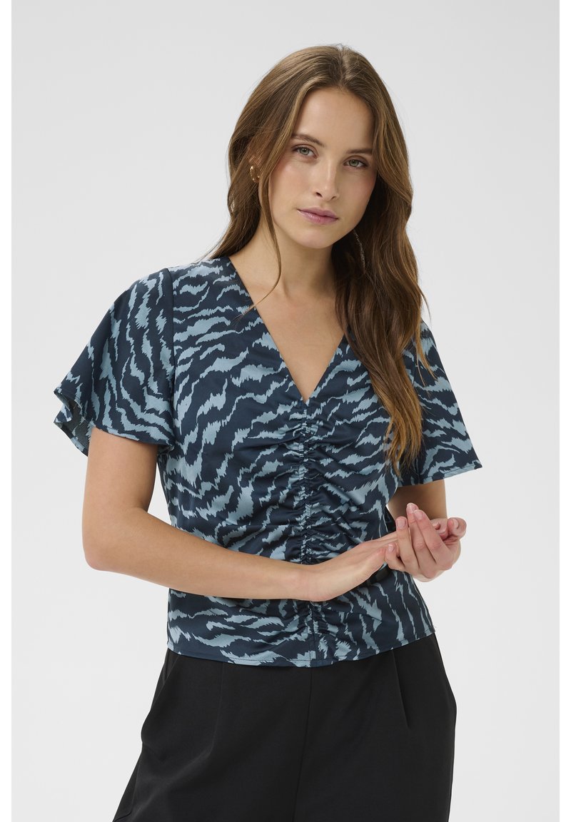 Top s krátkými rukávy v tmavě modrém a světle modrém vzoru. Má výstřih do V a na přední straně nashromážděné detaily. Lehká látka.