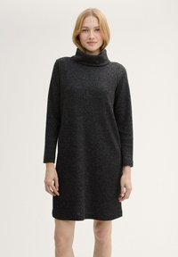 Schwarzes Pulloverkleid mit hohem Kragen, strukturiertem Stoff, langen Ärmeln und geradem Schnitt, das oberhalb des Knies endet.