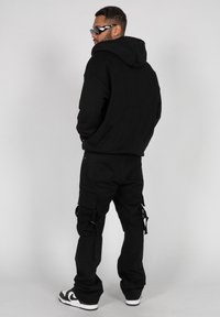 Svart hettegenser med stor hette, kombinert med svarte cargo-bukser med sidelommer og stropper. Brukt med hvite joggesko.