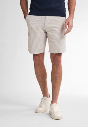 Light beige shorts with vertical pinstripes, made of soft fabric. Features side pockets and a relaxed fit. Paired with white sneakers.