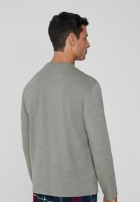 Šedé tričko s dlouhým rukávem vyrobené z měkké tkaniny. Má kulatý výstřih, rovný střih a minimalistický design bez viditelných log nebo vzorů.