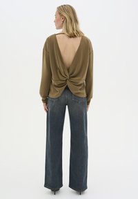 Maglietta olive green a maniche lunghe con scollatura a V e dettaglio torcigliato in vita, abbinata a jeans in denim scuro a vita alta e gamba larga.