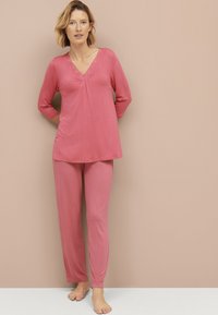 Een roze lounge-set bestaande uit een V-hals top met kantdetails en driekwartmouwen, gecombineerd met bijpassende lange broeken van een gladde stof.