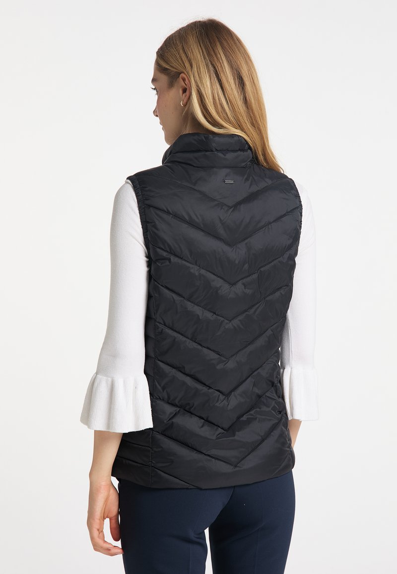 Schwarze Steppweste mit hohem Kragen, Chevron-Steppung und leichtem Material, getragen über einem weißen Langarmoberteil mit ausgestellt genähten Ärmel.