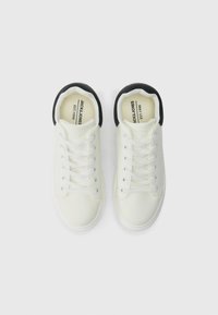 Hvite joggesko med jevn tekstur, avrundet tåparti, svart krage og seks par snørehull. Merkevarenavnet er synlig på innersålen.