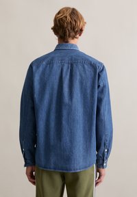 Denim overhemd met lange mouwen in donkerblauw, voorzien van een kraag en manchetten met knopen. De achterkant heeft een effen ontwerp met subtiele textuur en stiknaden.