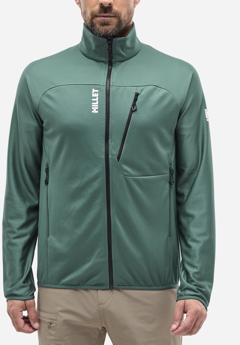 Grüne, durchgehende Jacke mit strukturierter Oberfläche, ausgestattet mit zwei seitlichen Taschen und einer Brusttasche mit schwarzen Reißverschlüssen. Logo auf der linken Seite.