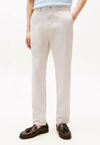 Pantaloni beige chiaro realizzati in tessuto liscio, con un design a gamba dritta e tasche frontali. Abbinati a mocassini marroni scuri con nappine.