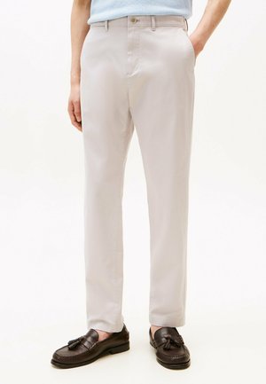 Lichtbeige broek van gladde stof, met een rechte pijpdesign en voorzakken. Gepaarde met donkerbruine mocassins met kwastjes.