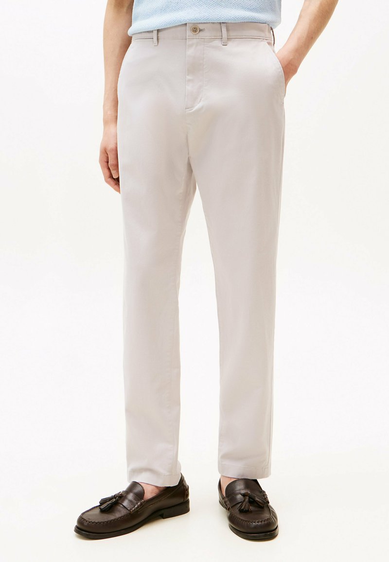 Pantaloni beige chiaro realizzati in tessuto liscio, con un design a gamba dritta e tasche frontali. Abbinati a mocassini marroni scuri con nappine.