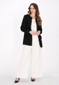Blazer din tweed negru cu accente albe, asortat cu pantaloni albi largi și pantofi cu toc negri. Blazerul are un finisaj texturat și buzunare.