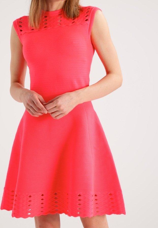 Robe sans manches ajustée de couleur rose vif avec une texture côtelée, présentant un motif découpé décoratif au niveau du col et une jupe évasée.