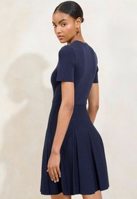 Marineblaues Kurzarmkleid mit taillierter Oberseite und plissiertem Rock. Weicher Stoff, Rundhalsausschnitt und dezente Rückendetails.