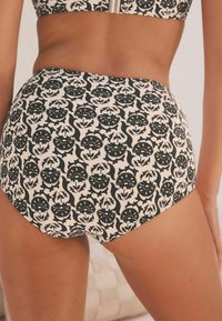 Schwarze und cremefarbene hochgeschnittene Bikiniunterteile mit einem komplizierten Blumenmuster, glatter Textur und passgenauer Form.