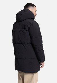 Chaqueta de plumón negra con capucha, que presenta un diseño acolchado y un ajuste holgado. Fabricada con un tejido suave de textura ligeramente brillante.