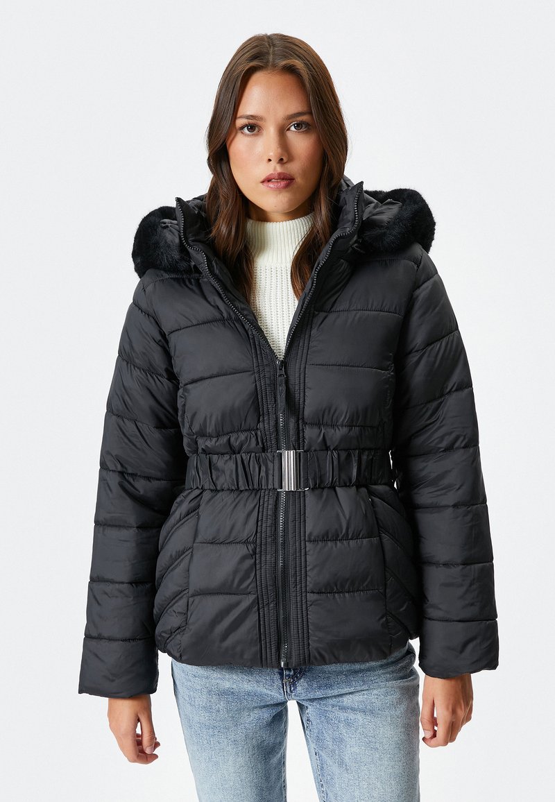 Schwarze gepolsterte Winterjacke mit Reißverschlussfront, tailliertem Gürtel und Kunstfellbesatz an der Kapuze. Verfügt über ein gesteppte Muster und lange Ärmel.