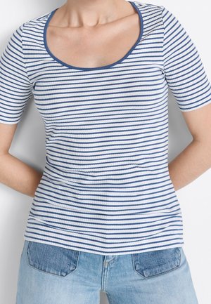 Vrouw draagt een wit en blauw horizontaal gestreept shirt met korte mouwen en een ronde hals, gecombineerd met lichtblauwe spijkerbroek.