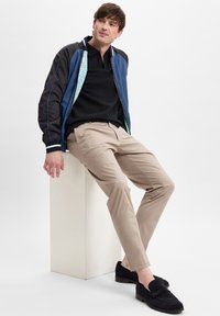Blue and black bomber jacket, black polo shirt, beige trousers, and black suede loafers. The jacket has a patterned lining and contrasting stripes.