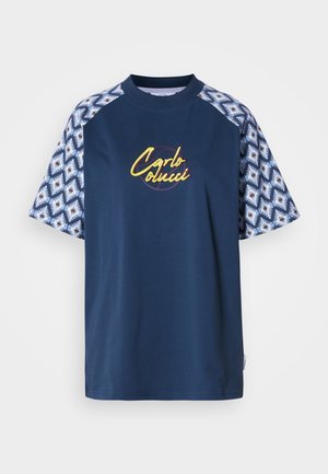Tumesinine lühikeste varrukatega t-särk mustriga varrukatega; esiküljel on kollane tikitud "Carlo Colucci" logo. Sile tekstuur, ümar kaelus.