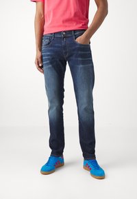 Mörkblå denimjeans med blekta detaljer och fem fickor, ihop med ljusblå sneakers med röda ränder och en gummisula.