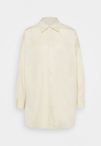 Chemise jaune pâle à boutons, fabriquée dans un tissu lisse, avec un col pointu et des manches longues légèrement bouffantes. Aucun motif visible.