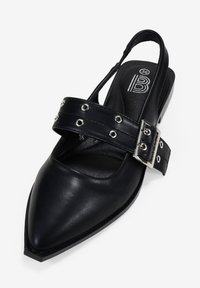 Scarpa slingback in pelle nera con punta affusolata, ampia cinghia decorata da borchie e fibbia in argento, suola piatta, texture liscia. Taglia 36 visibile all'interno.