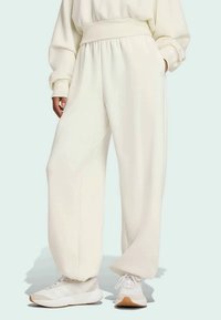 Λευκά, φαρδιά φόρμα με ψηλή ελαστική μέση και στενές μανσέτες, κατασκευασμένα από μαλακό ύφασμα, συνδυασμένα με ελαφριά αθλητικά παπούτσια.