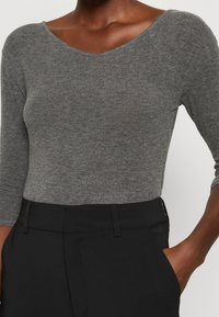 Grå, åtsittande bodysuit med lång ärm och bred halsringning, kombinerad med högmidjade svarta byxor som visar upp ett snyggt tyg och rena linjer.