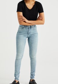 Ljusblå högmidjade skinny jeans i denim, med en klassisk femficksdesign och subtila blekningar. Parafraserat med en svart V-ringad topp.