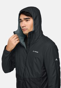 Veste noire avec capuche, dotée d'une doublure en polaire douce à l'intérieur. Fermeture éclair à l'avant, logo sur la poitrine, et accents contrastants sur les manches.