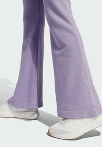 Rozšírené fialové tepláky vyrobené z mäkkej látky, skombinované s bielymi teniskami s šedými akcentami a gumovou podrážkou.