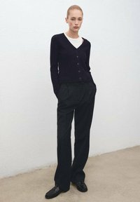 Cárdigan de punto azul marino con escote en V y detalle de botones, combinado con pantalones de pinstripe negros de cintura alta y mocasines negros.