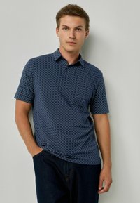 Trumpas rankovėmis tamsiai mėlynas polo marškinėliai su rombų raštu, pagaminti iš lygaus, tekstūruoto audinio. Savybės: apykaklė ir priekis su mygtukų užtrauktuku.