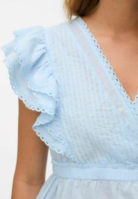 Robe bleu clair avec des manches volantées, ornée de rayures verticales et d'une bordure en dentelle le long du col et des bords de manches. Détail de taille élastique.