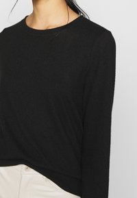 Svart långärmad topp med rund halsringning, med en mjuk textur och avslappnad passform, i kombination med ljusa byxor.