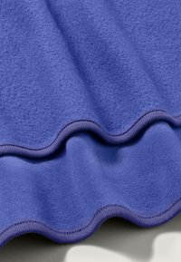 Lila fleece-tyg med en mjuk textur, med en vågig kant och kontrasterande sömdetalj längs kanten.