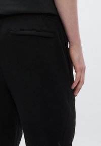 Μαύρο παντελόνι με λεία υφή που διαθέτει ραμμένη πίσω τσέπη. Η μέση είναι ελαστική και το σχέδιο είναι προσαρμοσμένο για άνεση.