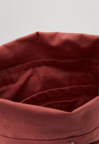 Rote Canvas-Tasche mit weichem Stofftextur, ausgestattet mit abgerundetem oberen Rand und Innenfächern. Doppelt genähten Naht sichtbar entlang der Öffnung.